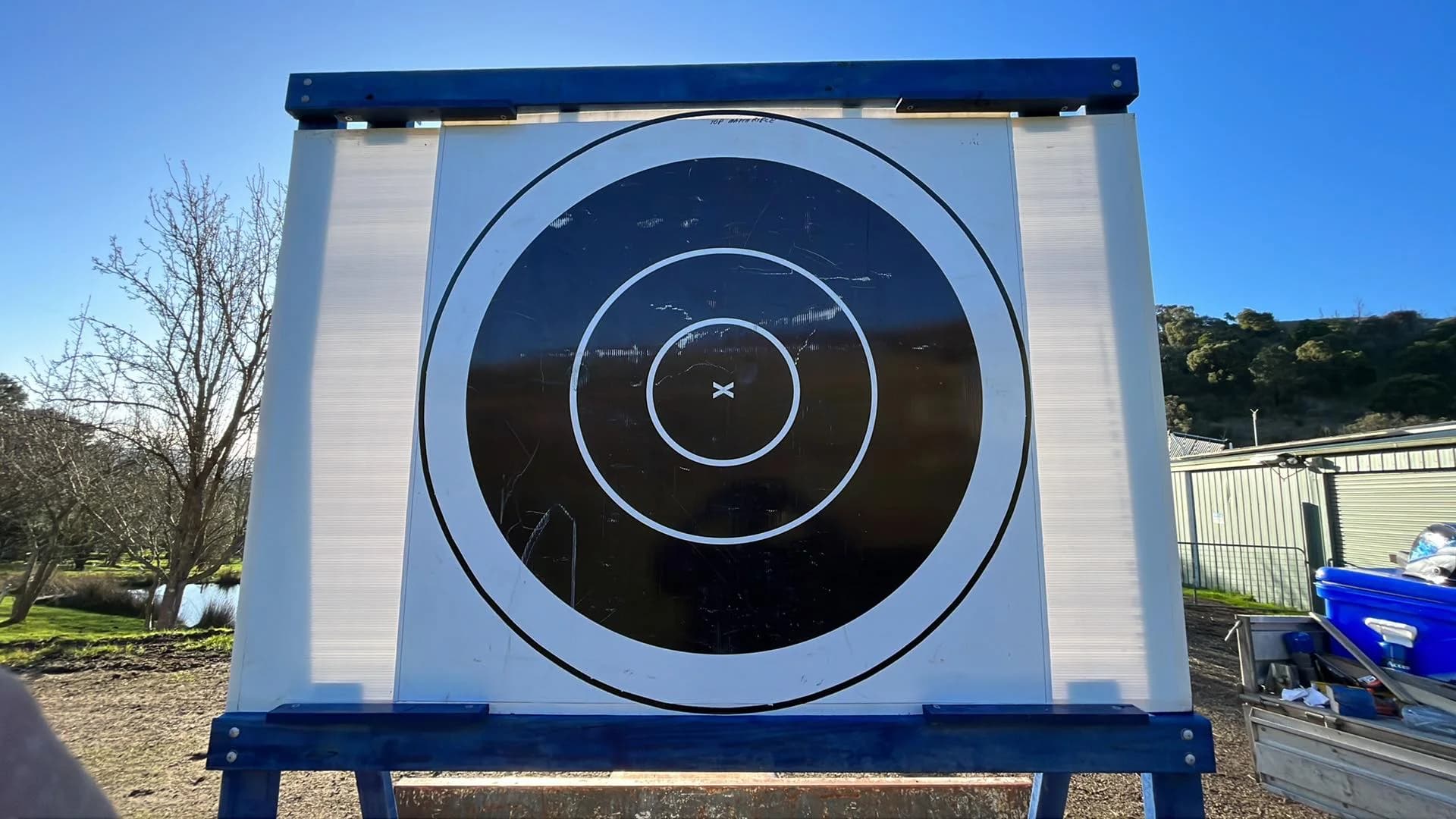 A large circular target face mounted in a blue steel frame outdoors.