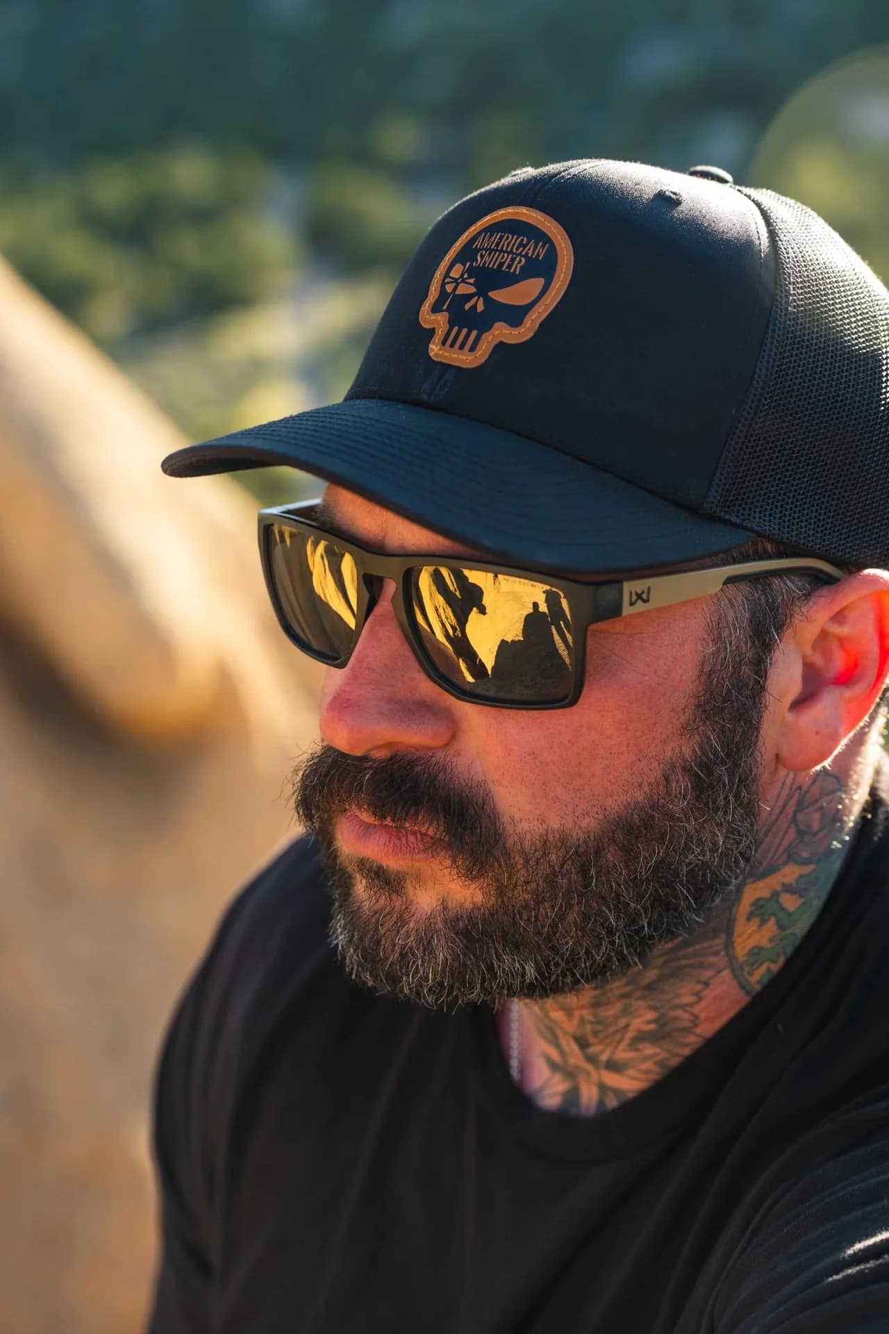 A man in an American Sniper cap and sunglasses in golden evening light.