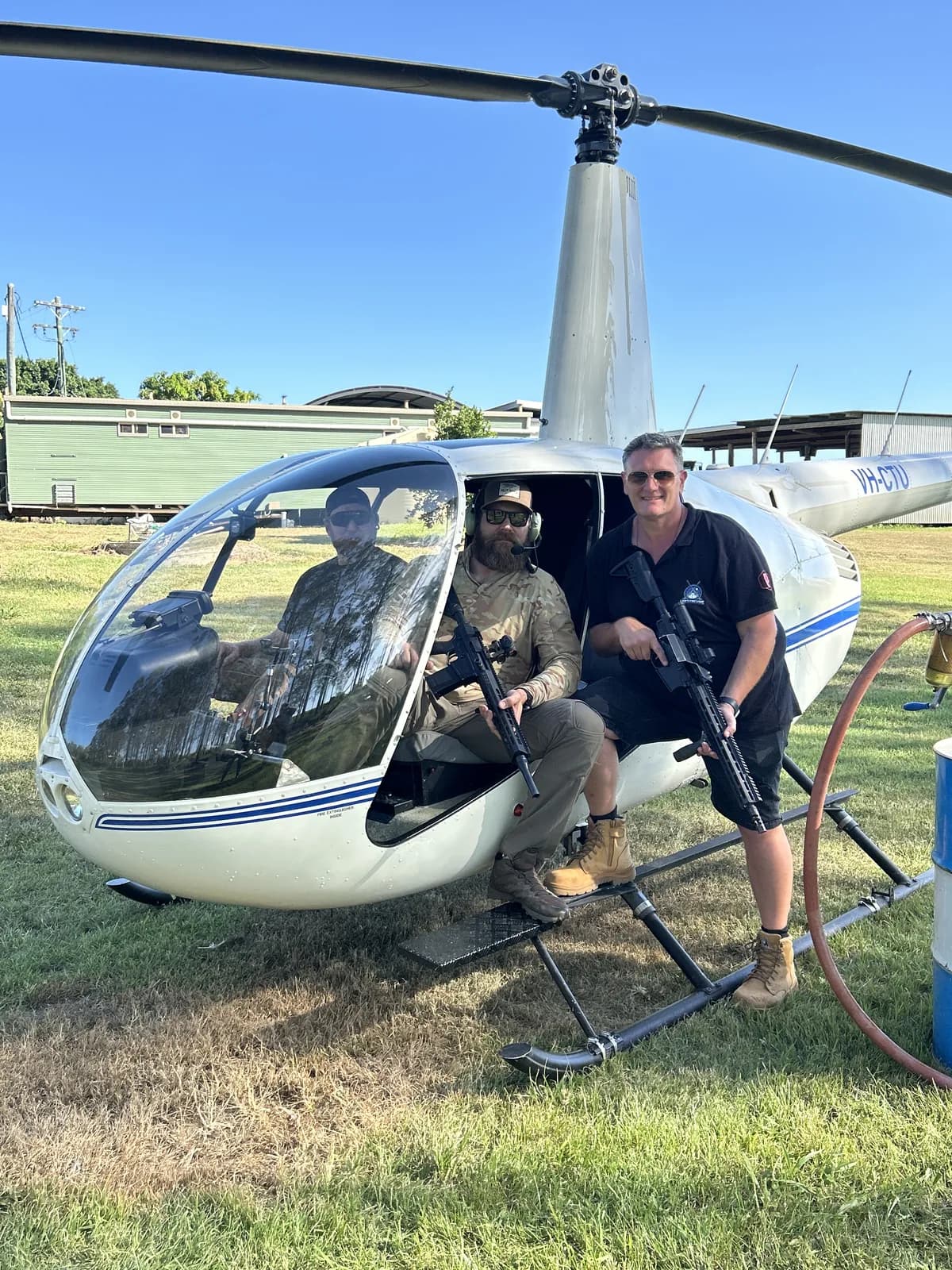 Wayne Lording holding a rifle beside a helicopter used for aerial pest control.