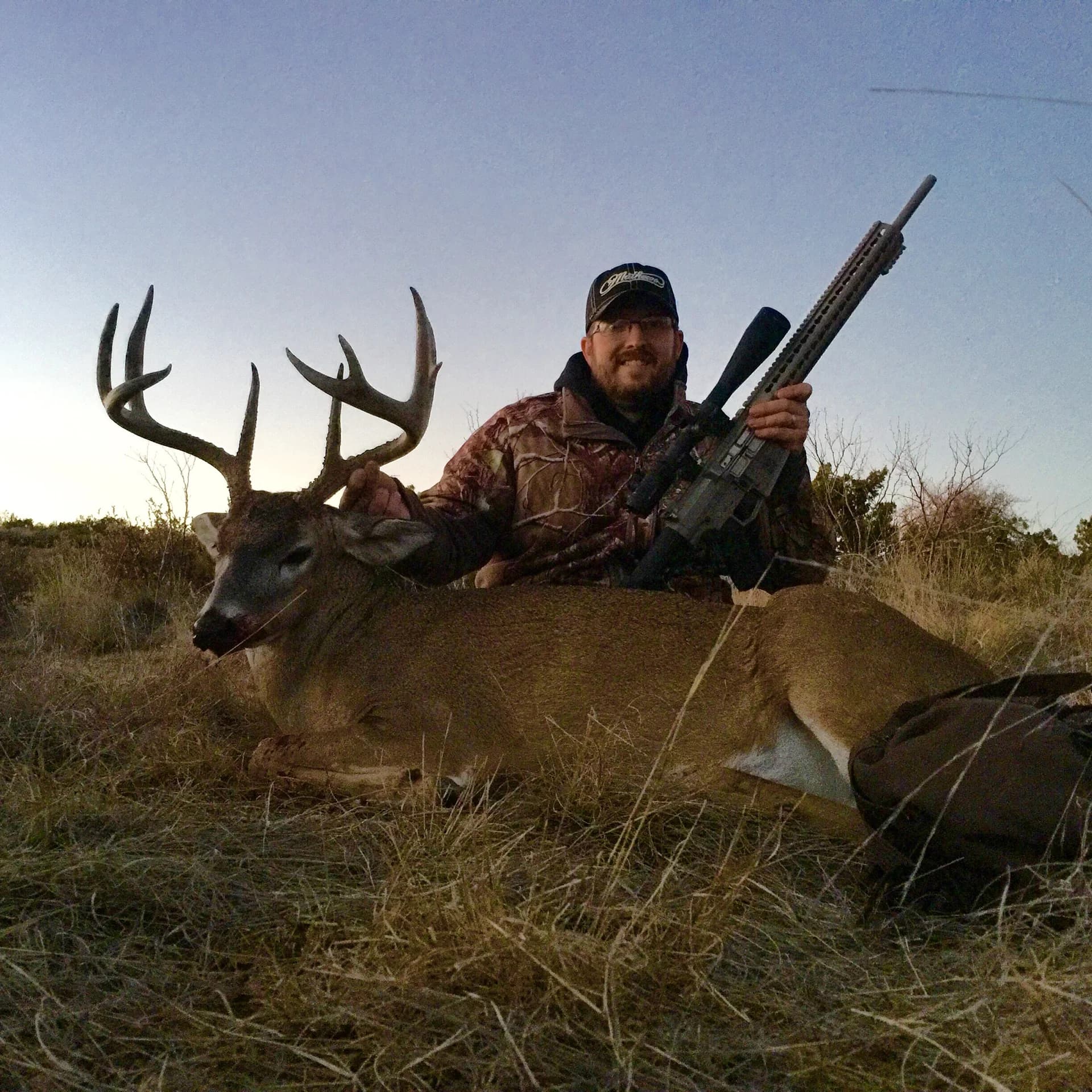 A hunter with a WMD Guns rifle and a whitetail buck at dusk.